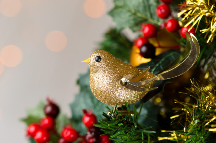 Festive Christmas close up of tree decorated with gold glitter robin, tinsel and holly berries. Bokeh copy space.