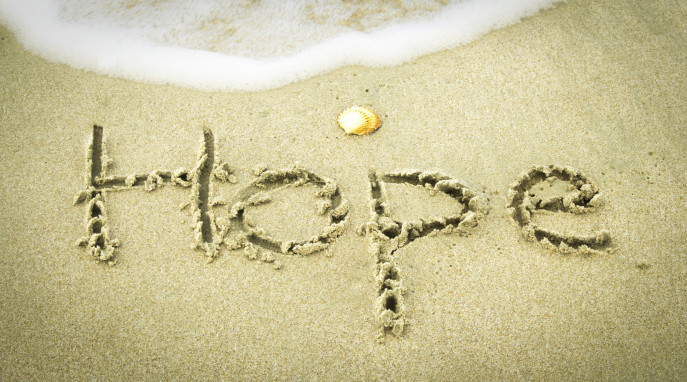 Word "Hope" handwritten in sand at beach.